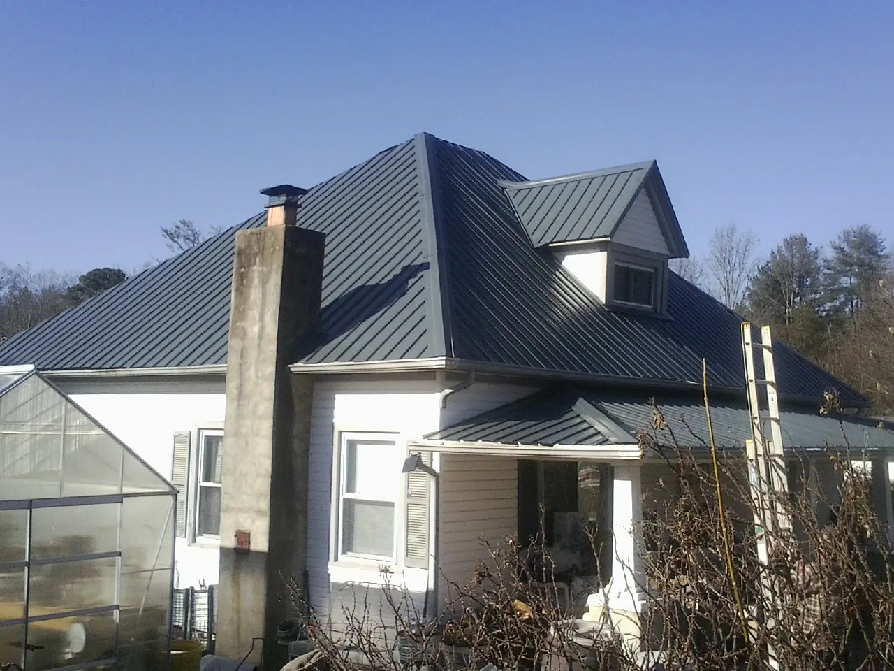 Dark blue standing seam metal roof on a white farmhouse with dormer — Slate & Tile Roof Repair by Roofing Brothers in La Mirada
