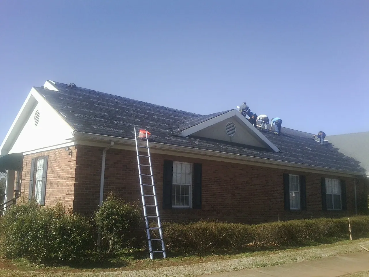Crew tearing shingles off a brick ranch roof with a ladder set — Emergency Roof Repair work by our crew in La Mirada