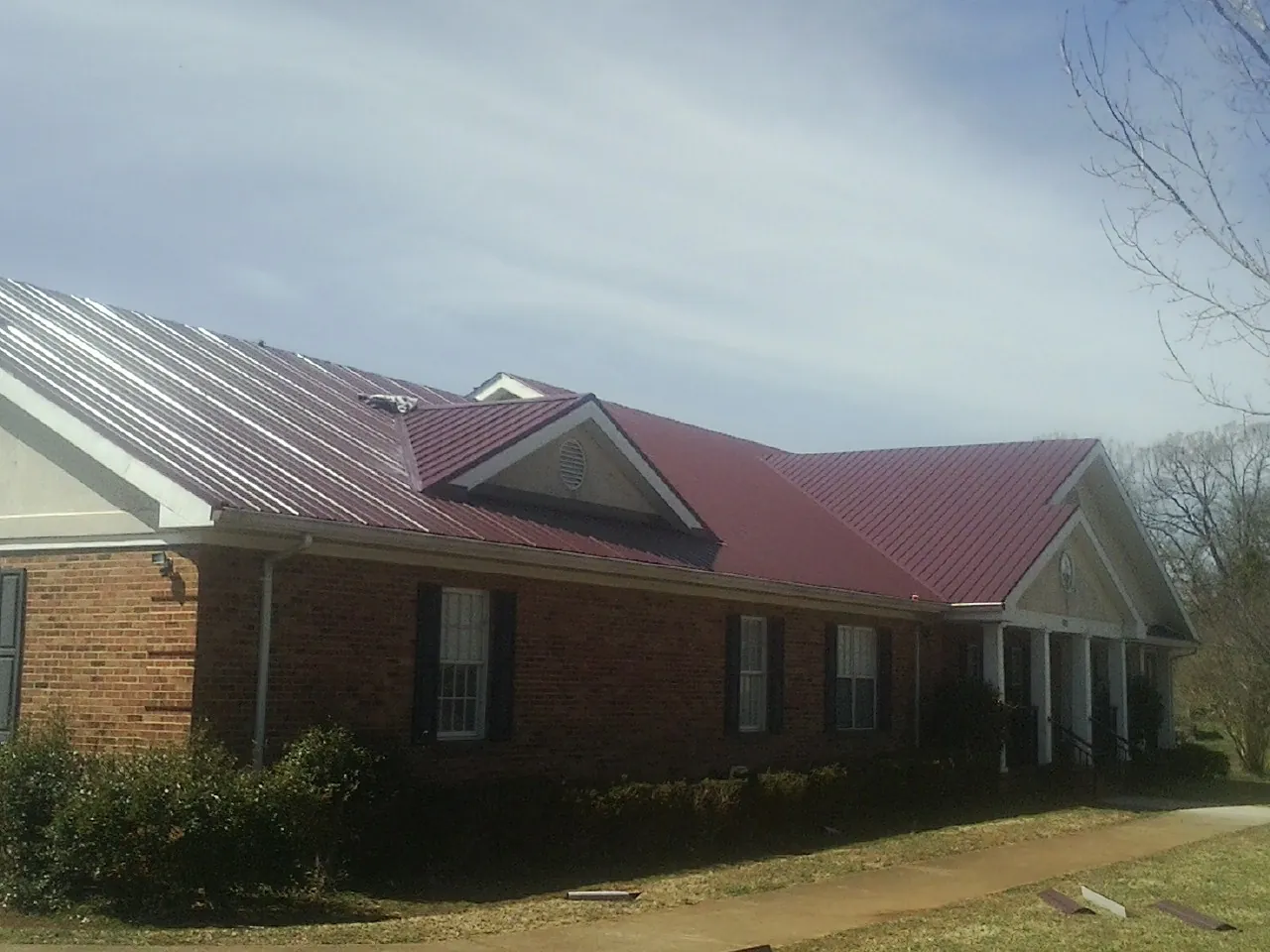 Red metal roof with gabled entries on a long brick building, from a Hail Damage Roof Repair job in La Mirada