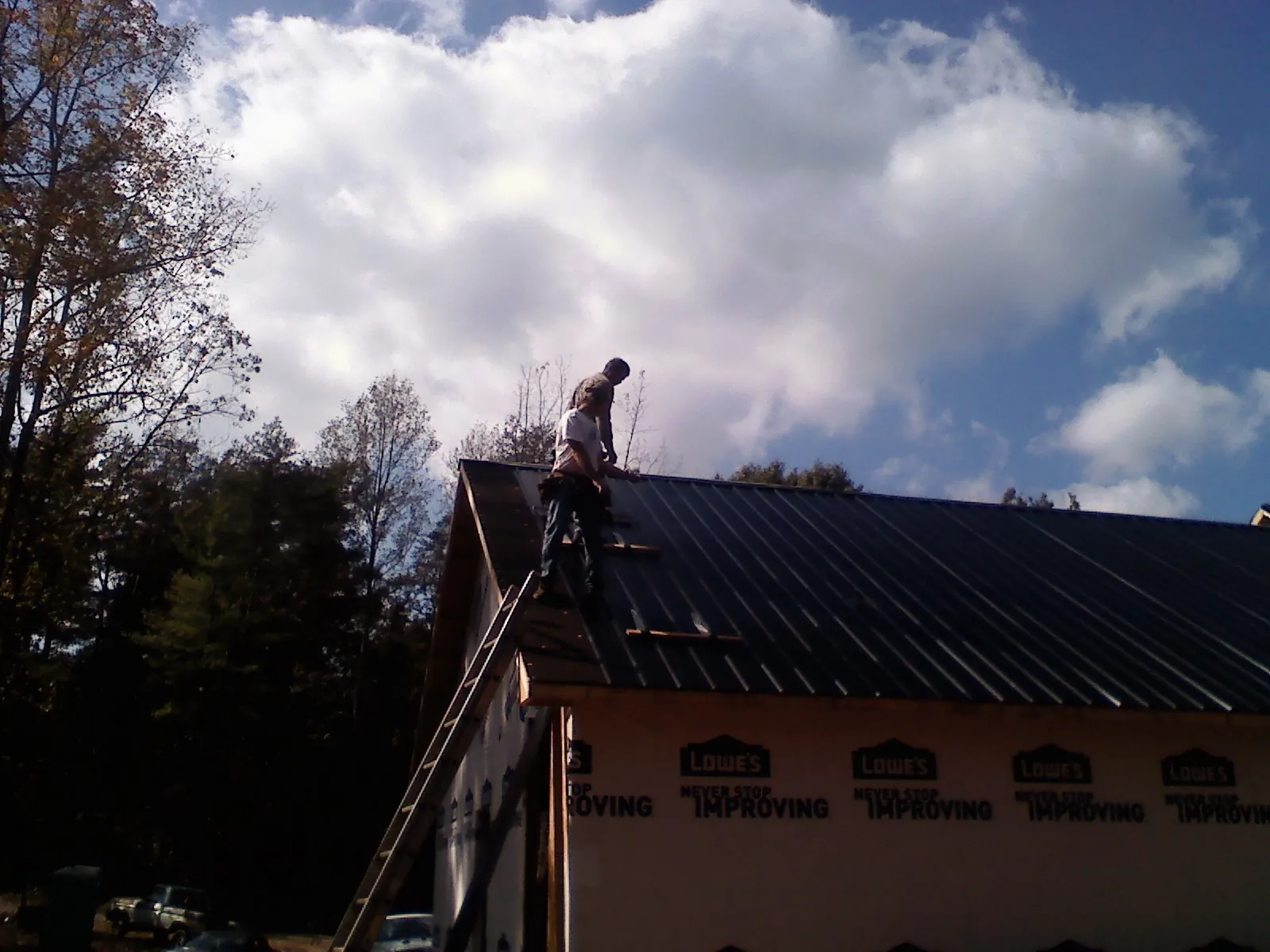 Roofer fastening dark metal panels high against a cloudy sky, from a Roof Inspection job in La Mirada