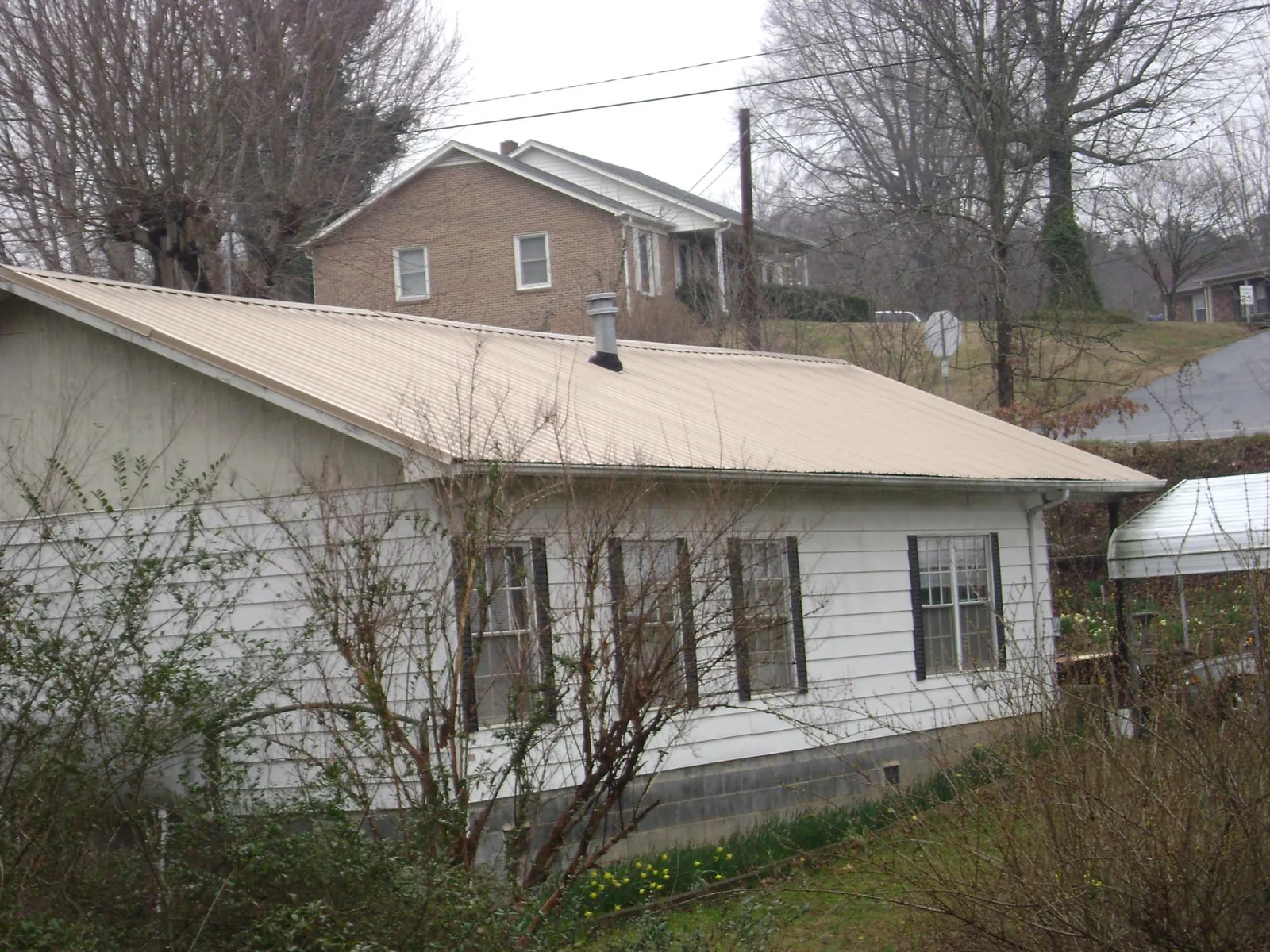 Tan metal roof on a white sided house set into a hillside — Commercial Roofing by Roofing Brothers in La Mirada